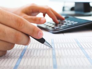 Une main sur la calculatrice, l'autre main tenant un crayon et prenant des notes sur une feuille de chiffres. Cette image représente le programme Comptabilité et gestion.