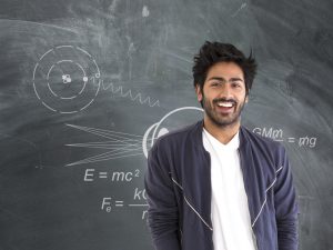 Jeune homme devant un tableau avec des calculs et des formules. Image représentant les sciences naturelles et appliquées.