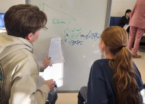 Une étudiante et un étudiant de la brigade de Maisonneuve en Commun tente de résoudre une équation mathématique sur un tableau blanc.