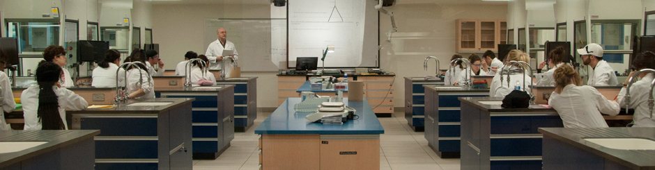 Étudiants dans une classe laboratoire. Un prof à l'avant de la classe leur enseigne la matière.