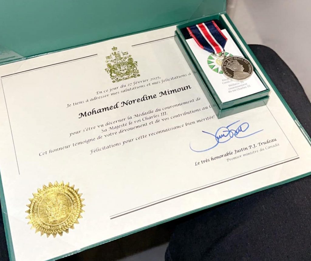 Certificat en angle avec le nom Mohamed Noredine Mimoun avec le sceau en or et signé par Justin Trudeau. Sur le certificat, une petite boite avec la médaille du Charles 3e