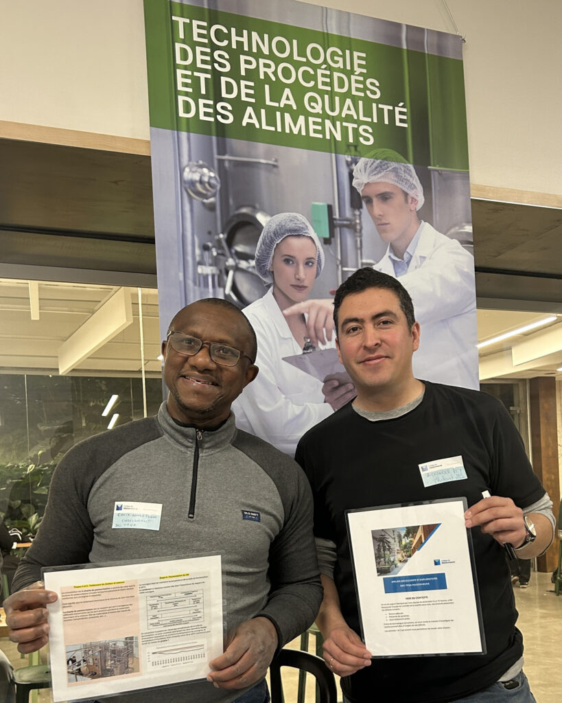 L'enseignant Cheik Ahmed Touré posant fièrement avec un étudiant devant le kiosque de leur programme Technologie des procédés et de la qualité des aliments lors de la soirée des Portes ouvertes du 18 novembre 2025.