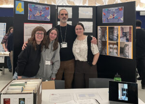 Deux étudiantes et leur enseignant en Techniques de la documentation et une intervenante du milieu, qui posent fièrement devant leur kiosque lors de de la présentation de leur projet.