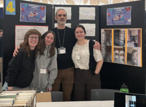 Deux étudiantes et leur enseignant en Techniques de la documentation et une intervenante du milieu, qui posent fièrement devant leur kiosque lors de de la présentation de leur projet.